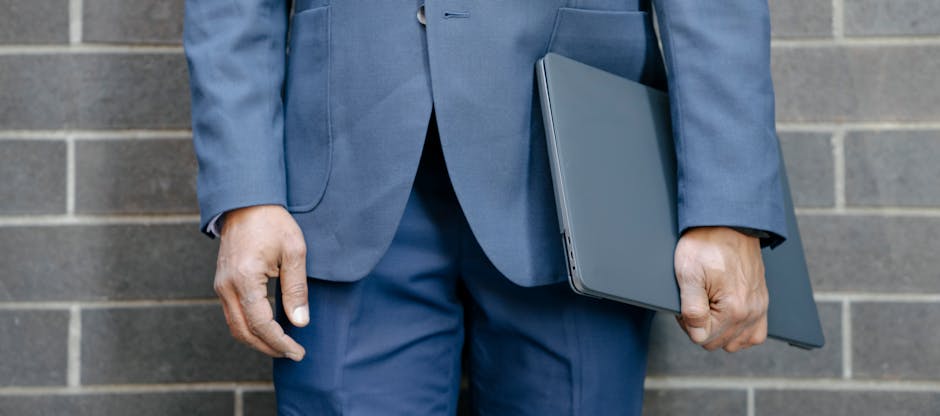 Close-up of a businessman in a blue suit holding a laptop against a brick wall