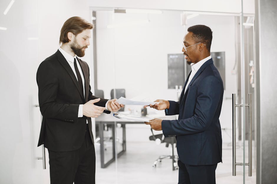 Two businessmen in formal suits exchanging documents in a modern office setting, symbolizing collaboration and partnership