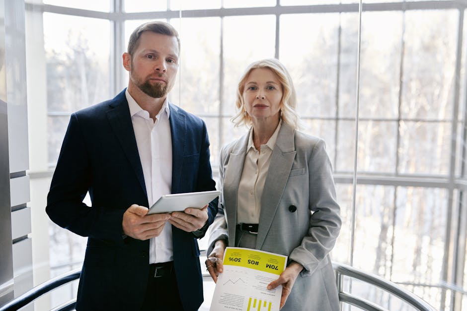 Two business professionals in a modern office discussing a project with a tablet and report